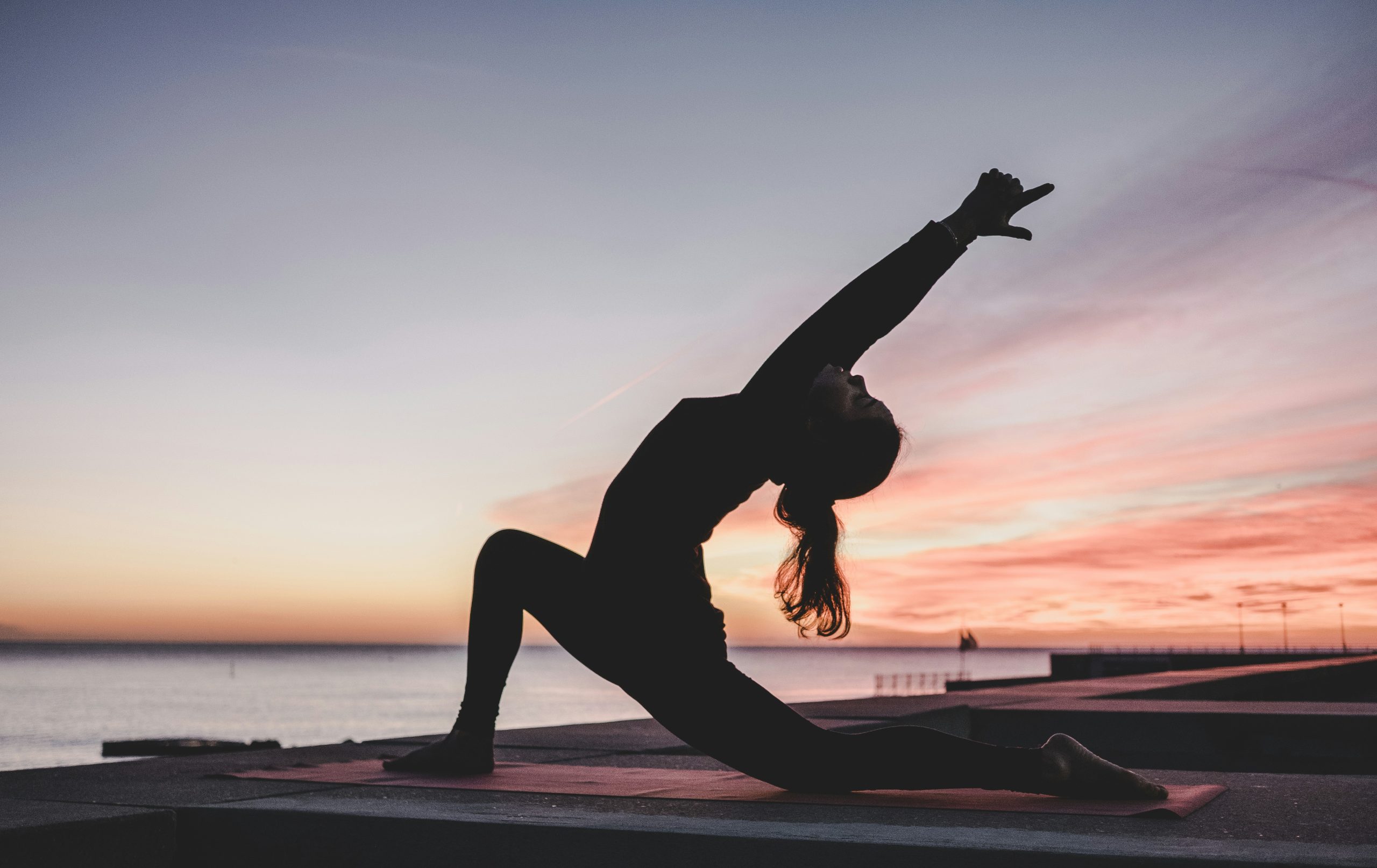 Alexis Faye practicing yoga at sunrise by the water, holding a low lunge backbend pose on a yoga mat during an outdoor yoga session